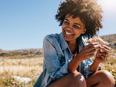 Woman smiling while eating healthy sandwich outside