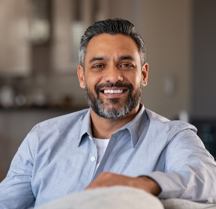 Man sitting on couch smiling with dental implants in Mississauga