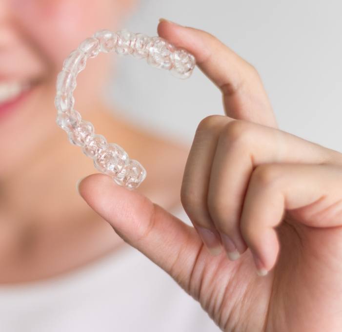 Smiling person holding Invisalign clear aligner in Mississauga