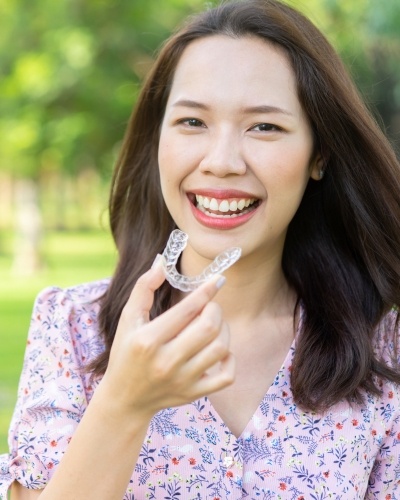 Smiling woman holding an Invisalign aligner outdoors