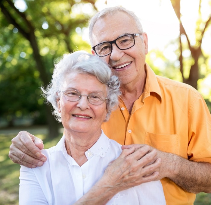 Senior man and woman smiling outdoors after replacing missing teeth in Mississauga