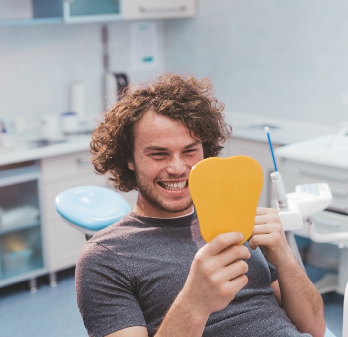 Dental patient looking at his smile in mirror after dental services in Mississauga