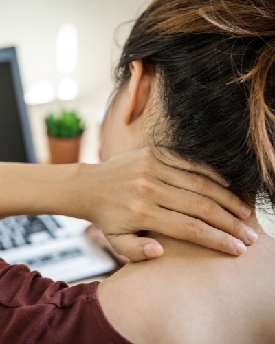 Woman sitting at desk with her hand on the back of her neck