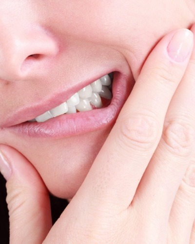 Close up of person wincing and holding their jaw in pain